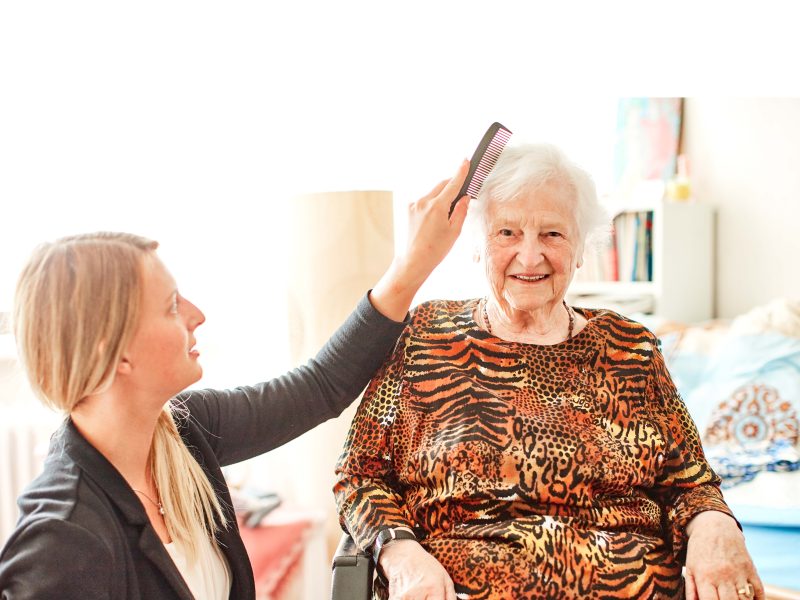 Eine ambulante Pflegerin kämmt einer Patientin die Haare in ihrer Wohnung